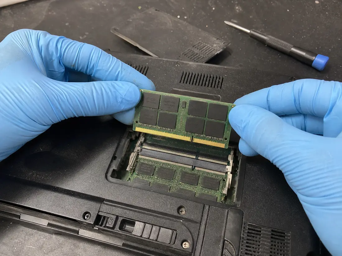 Модуль пам'яті SO-DIMM, який тримають за краї над відкритими слотами RAM у ноутбуці